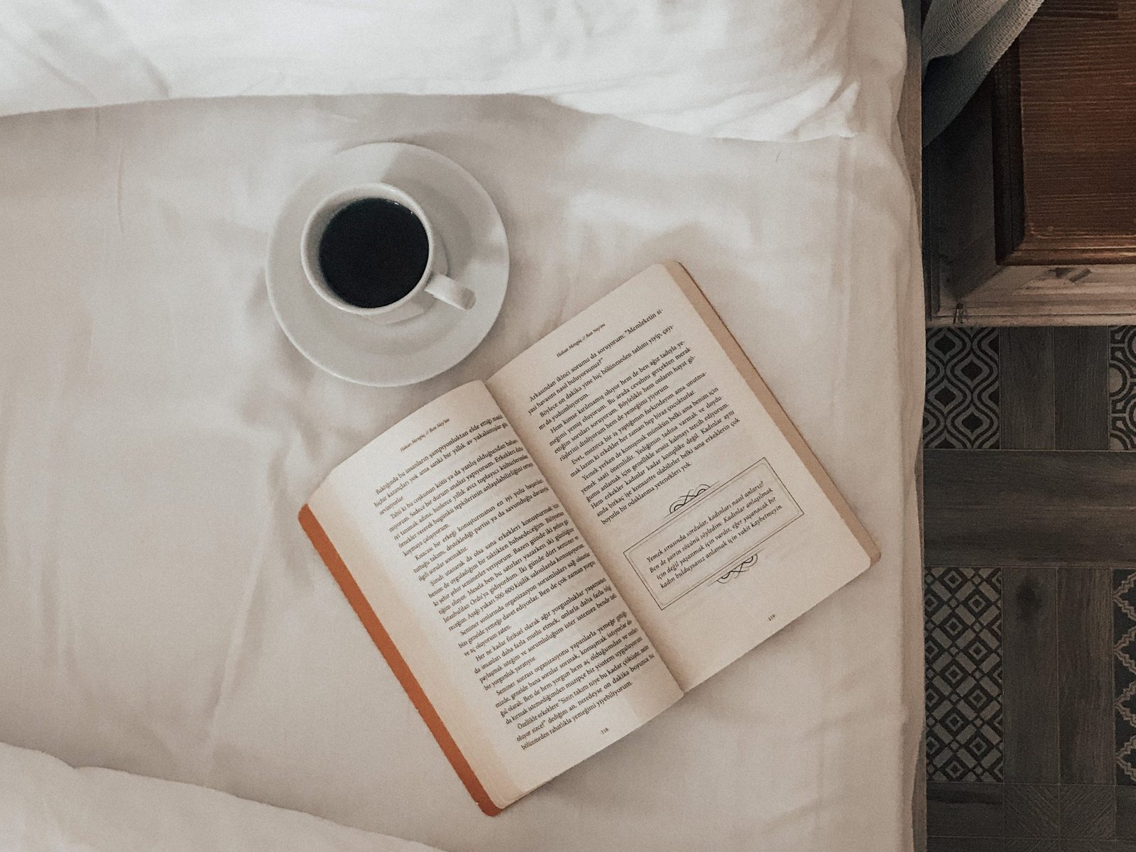 a-book-with-a-cup-of-coffee-on-bed-with-white-sheet